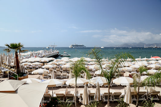 Beach scene with white umbrellas and boats in the background. Bring the luxury and vibe of the celebrated Carlton Beach Club into your abode. Buy framed wall art and French Riviera Fine Art Prints. Cannes Carlton Hotel.