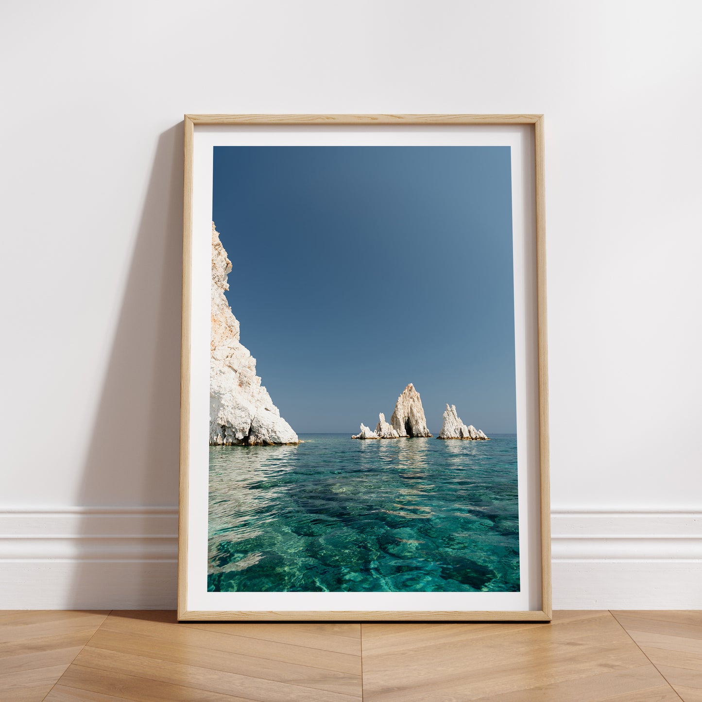 Greek Islands art print schowcasing vibrant blue portrait image of rocks at and ocean at Polyaigos Island near Milos. Wood frame mock up of Greece fine art photographic print.