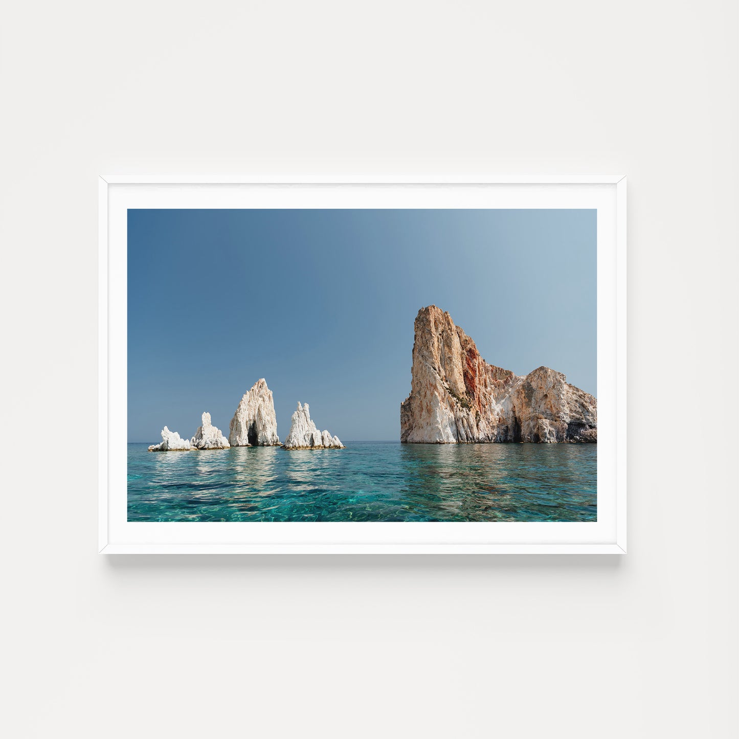 Greek Islands art print schowcasing vibrant blue landscape image of rocks and ocean at Polyaigos Island near Milos. White frame mock up of Greece fine art photographic print.