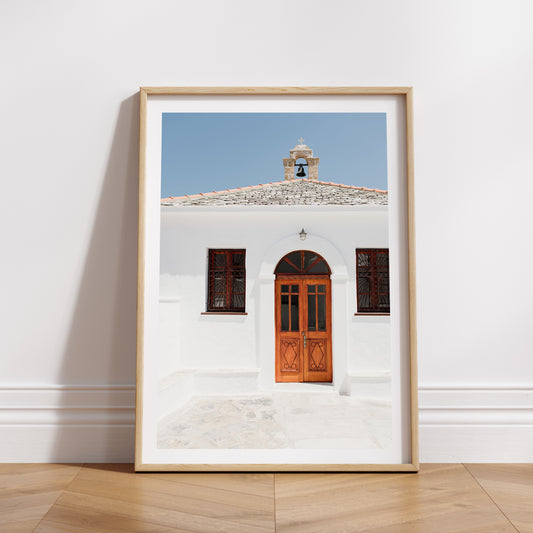 Framed photograph of a white building with a wooden door on a wall.