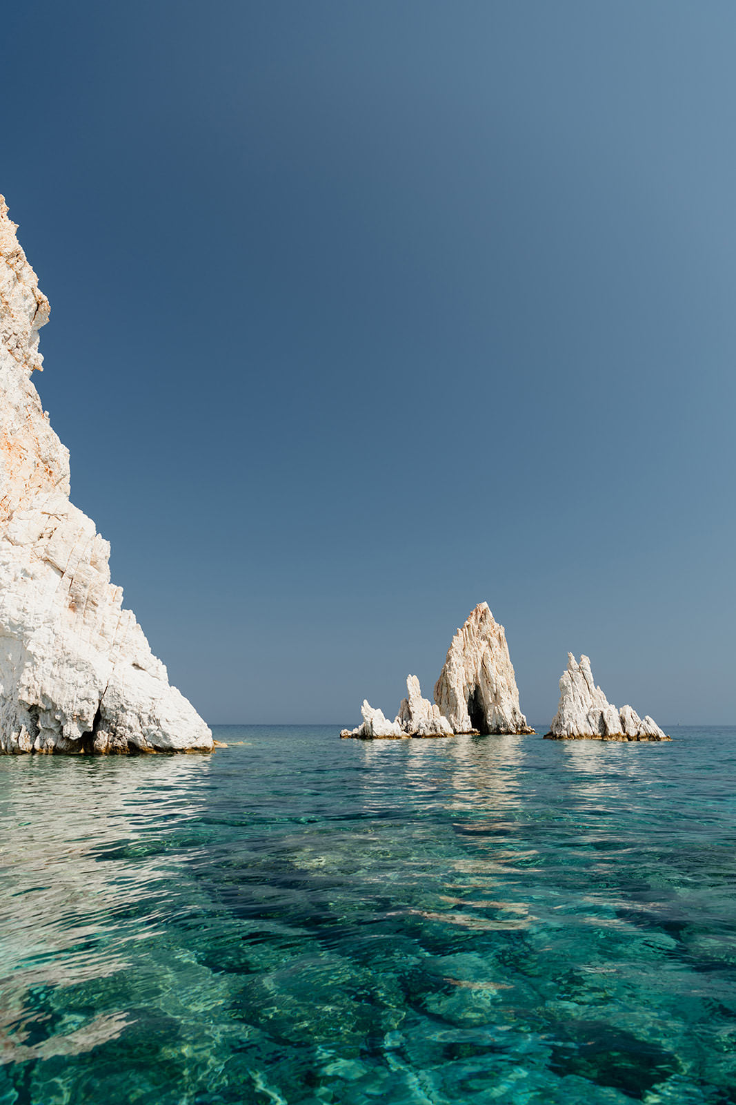 Greek Islands art print schowcasing vibrant blue portrait image of rocks at and ocean at Polyaigos Island near Milos. High quality Greece fine art photographic print available for purchase.