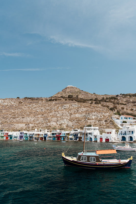 Photograph of a coastal scene with a boat in the water and a mountainous landscape. MILOS ISLAND, GREECE | SHOP Milos Photography Prints, bring the summer and colour of Greece into your home. Milos Photography Art Prints.
