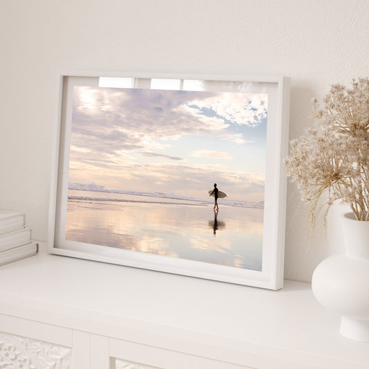 Coastal Australian fine art print featuring surfer walking along glassy sand on a Queensland beach at sunrise. Mocked up in a white frame, landscape format and sold as a coastal Australian fine art print.