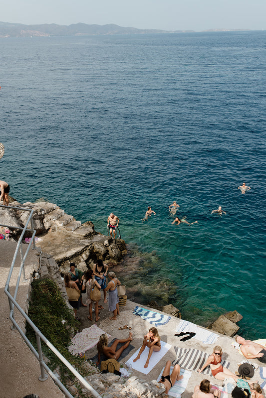 Photograph of a coastal scene with people by the sea. HYDRA ISLAND, GREECE. SHOP Mediterranean Fine Art Prints and bring the love of summer in the Med into your home. Med Swims and Med Art Prints.