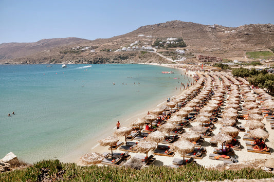 Beach scene with rows of umbrellas and mountains in the background. Mykonos Beach Club Wall Art Prints.