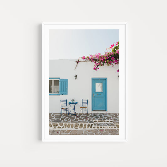 White wall with blue door and shutters, pink flowers, and outdoor furniture. ANTIPAROS, CYCLADES ISLANDS, GREECE Wall Art Prints. Adorn your walls with quaint Greek Islands scenes from Antiparos. Shop Greece Art Prints. 