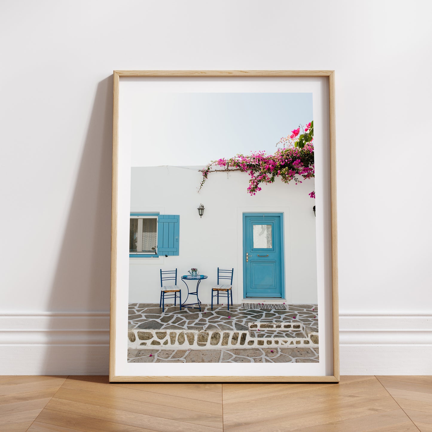 White wall with blue door and shutters, pink flowers, and outdoor furniture. ANTIPAROS, CYCLADES ISLANDS, GREECE Wall Art Prints. Adorn your walls with quaint Greek Islands scenes from Antiparos. Shop Greece Art Prints. 