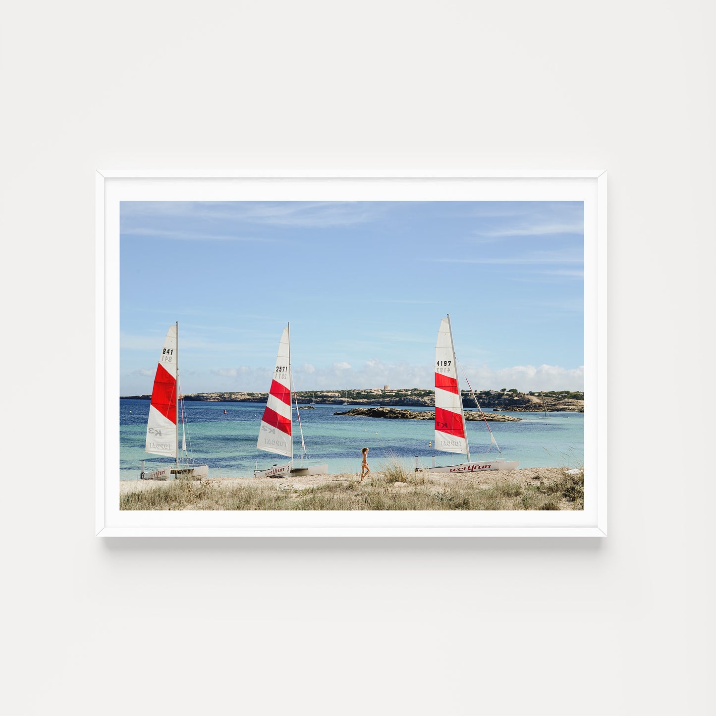 Framed photograph of three sailboats on a beach with a person walking towards them. SHOP fun and vibrant wall art prints featuring summer scenes in the Spain's Balearic Islands. Formentera Wall Art. Spain Fine Art Photographic Prints.