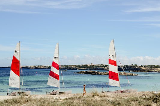 Framed photograph of three sailboats on a beach with a person walking towards them. SHOP fun and vibrant wall art prints featuring summer scenes in the Spain's Balearic Islands. Formentera Wall Art. Spain Fine Art Photographic Prints.