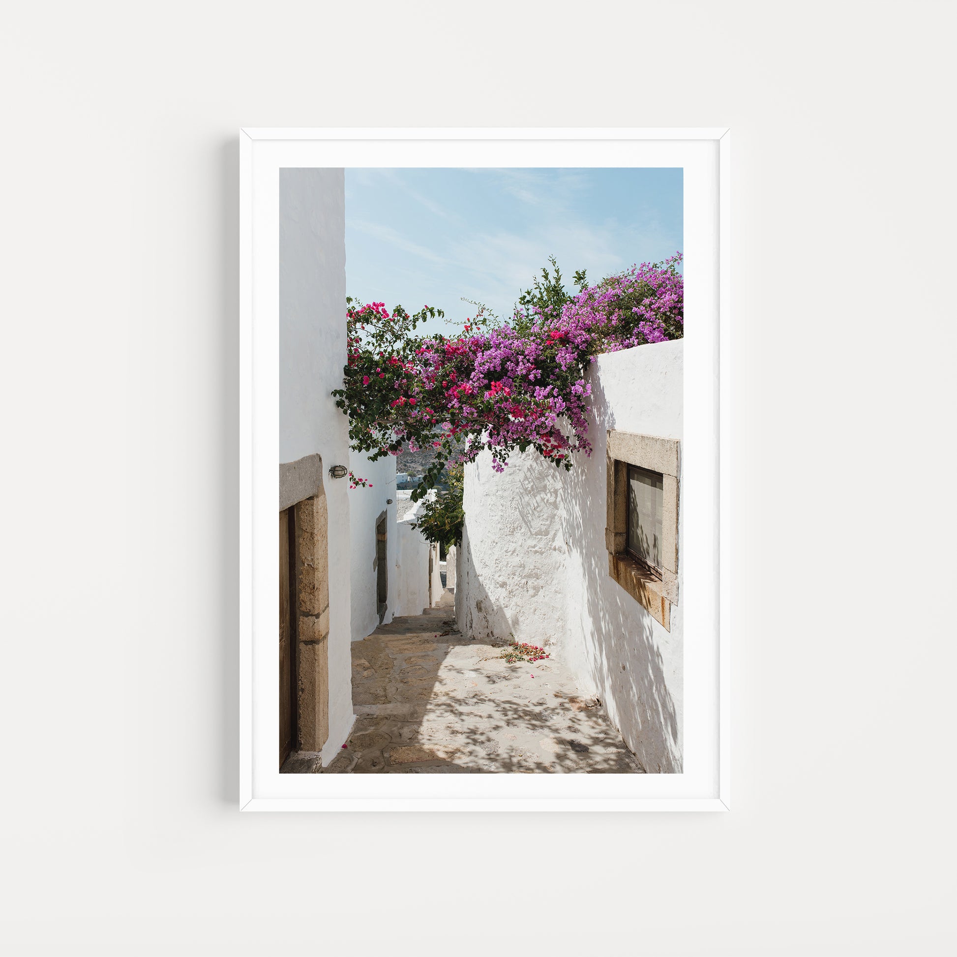 Narrow street with white walls and pink flowers in a Mediterranean setting. Bougainvillea Fine Art Photography Prints by Brooke Darling. Bring the floral dream of Greece into your home with Greek Island fine art photography prints.
