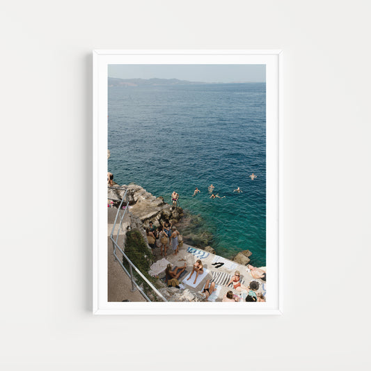 Framed photograph of a coastal scene with people by the sea. HYDRA ISLAND, GREECE. SHOP Mediterranean Fine Art Prints and bring the love of summer in the Med into your home. Med Swims and Med Art Prints.