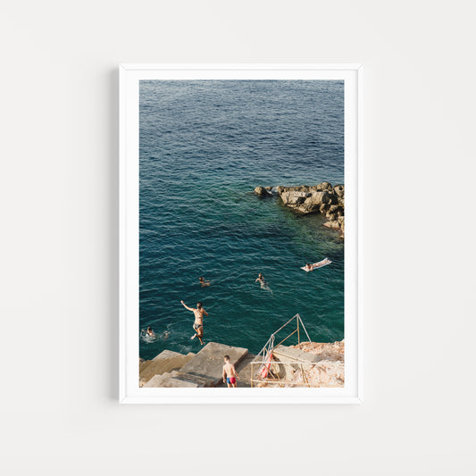 Framed photograph of people swimming and diving into the ocean from a rocky shore. HYDRA ISLAND, GREECE. SHOP | European Fine Art Photography Prints. Bring the spirit of European summers into your space. Europe Summer Photography Wall Art. 