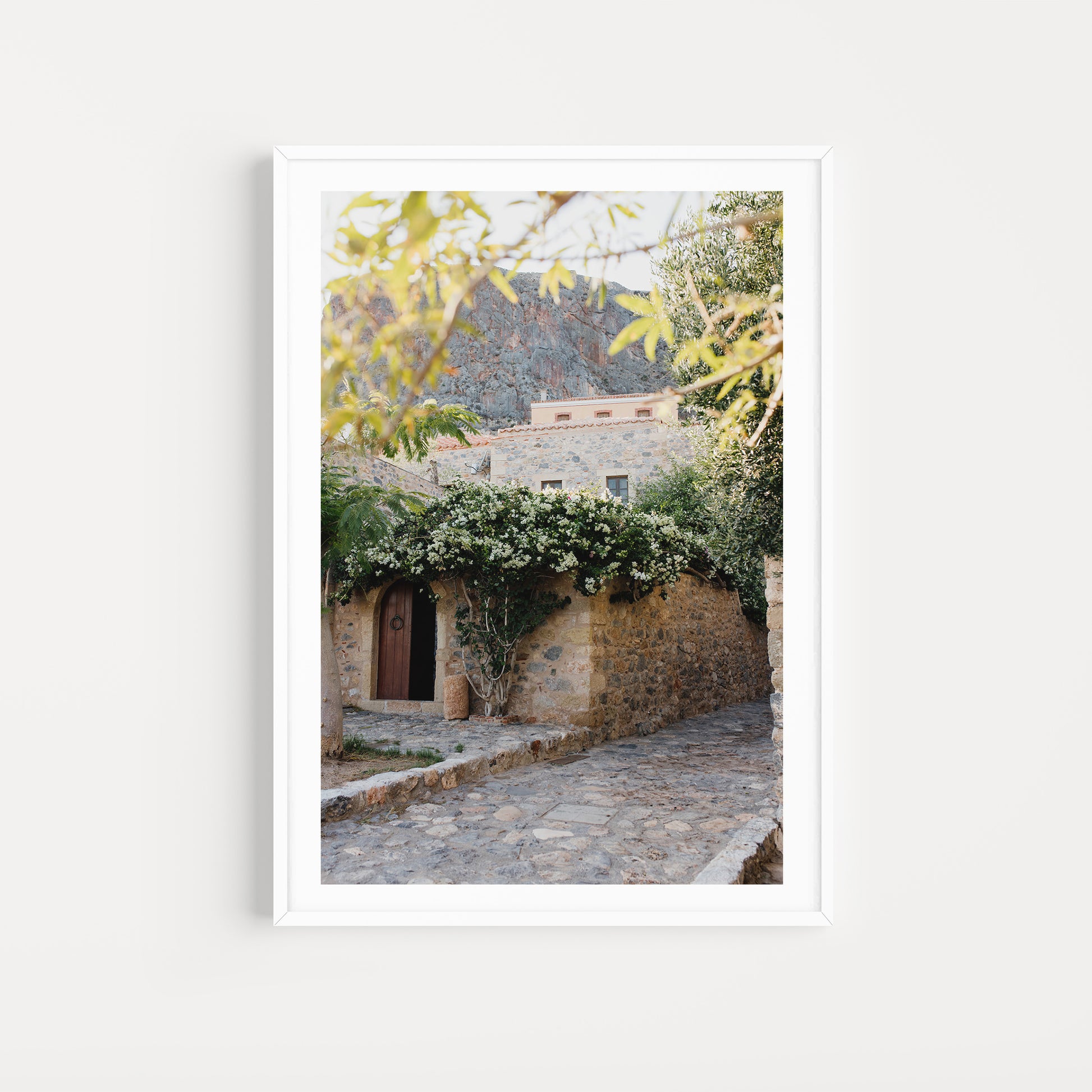 Framed photograph of a stone building with greenery on a white background. Greece wall art print collection boasts beautiful artwork featuring the beautiful coastal scenes of Monemvasia, Paros and more. Greece Photographic Wall Art.