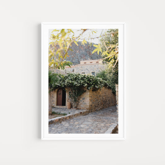 Framed photograph of a stone building with greenery on a white background. Greece wall art print collection boasts beautiful artwork featuring the beautiful coastal scenes of Monemvasia, Paros and more. Greece Photographic Wall Art.