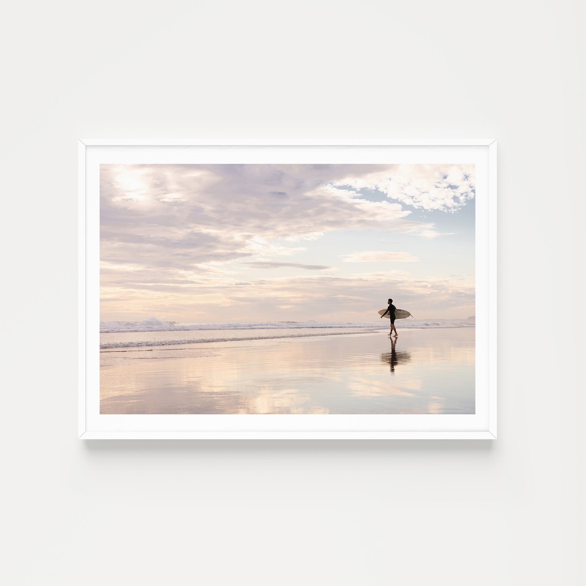 Coastal Australian fine art print featuring surfer walking along glassy sand on a Queensland beach at sunrise. Mocked up in a white frame, landscape format and sold as a coastal Australian fine art print. 