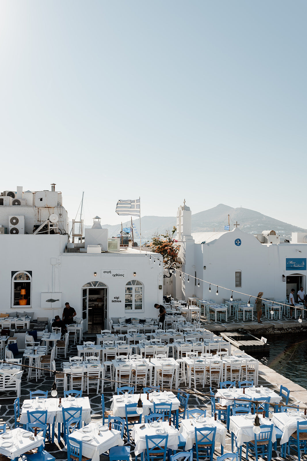 Greece Fine Art Photography Prints of an outdoor taverna on Naoussa boat harbour on the island of Paros. Portrait orientation. By Brooke Darling Photography.