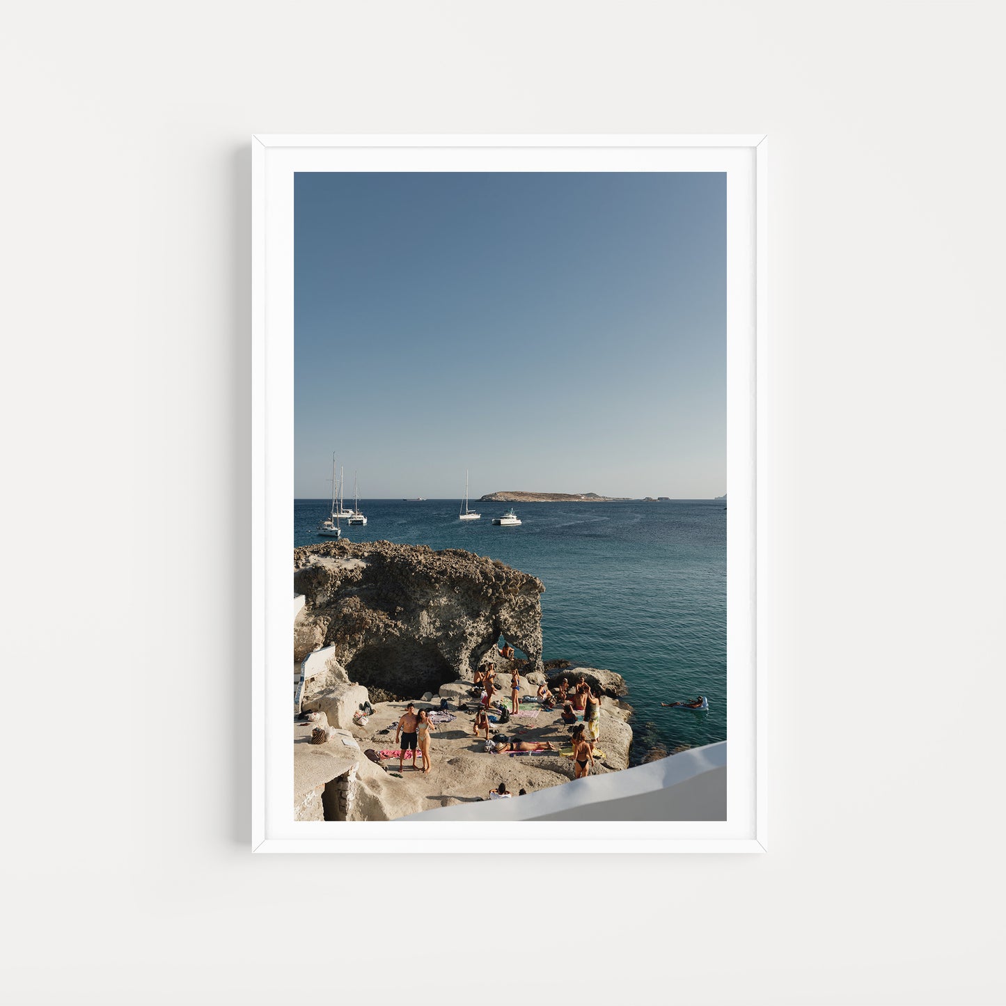Framed photograph of a scenic coastal view with people on rocks and boats in the distance. Shop Greece Art Prints with Kimolos friends on a rock. 