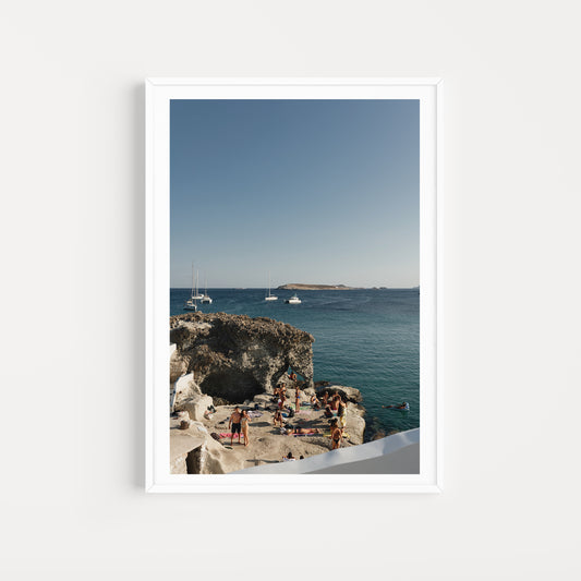 Framed photograph of a scenic coastal view with people on rocks and boats in the distance. Shop Greece Art Prints with Kimolos friends on a rock. 