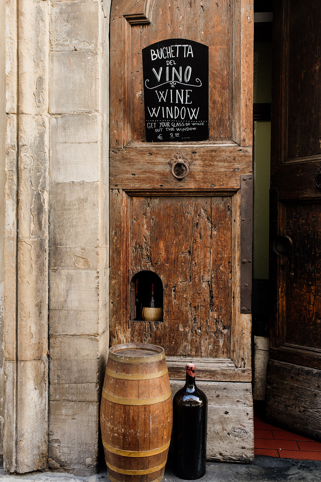 Wooden door with a wine-themed sign and barrel, bottle, and candle in front. FLORENCE, TUSCANY, ITALY | SHOP Tuscany Photographic Wall Art Prints. Transport yourself into the heart of wine culture with this Wine Art Photography Print. 