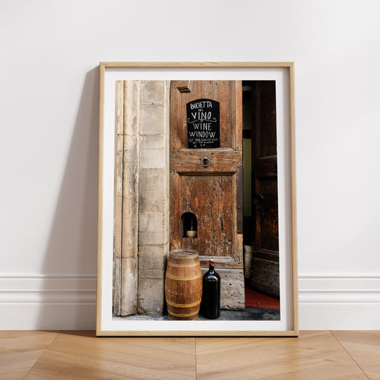 Wooden door with a wine-themed sign and barrel, bottle, and candle in front. FLORENCE, TUSCANY, ITALY | SHOP Tuscany Photographic Wall Art Prints. Transport yourself into the heart of wine culture with this Wine Art Photography Print. 