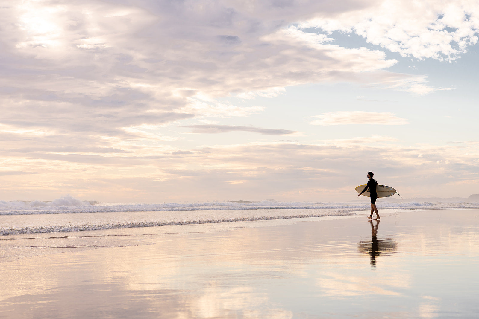 Coastal Australian fine art print featuring surfer walking along glassy sand on a Queensland beach at sunrise. Available in a white frame, landscape format and sold as a coastal Australian fine art print. 